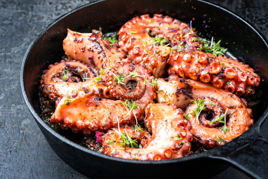 Traditional Spanish octopus braised cooked with tomatoes and herbs in wine sauce as closeup in a cast-iron saucepan