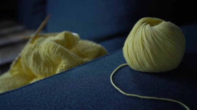 A skein of yellow cotton and an unfinished knitted sweater on a blue sofa. Slow motion