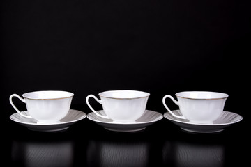 Three white tea cups stand on a table on a black background