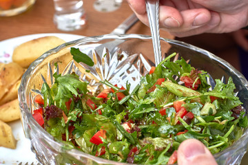 Vegetarian salad of arugula, herbs and tomatoes in a salad bowl in the hands