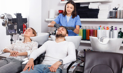 Portrait of woman hairdresser in gloves  washing hair of smiling man in salon