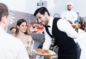 Waiter bringing seafood dishes in fish restaurant