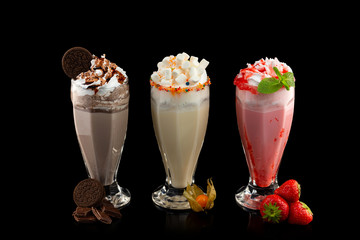Three glasses of colorful milkshake cocktails - chocolate, strawberry and vanilla decorated with...