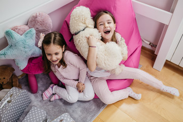 Cute little sisters playing with poodle in children's room.