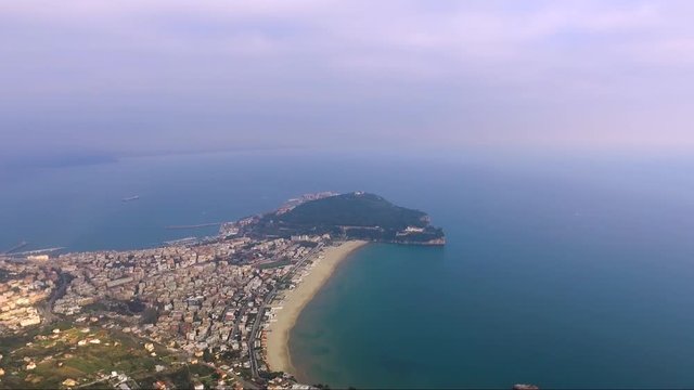 Aerial distant high angle slow approach down the coastline of Gaeta, Italy to the tree covered Parco Monte Orlando Concept: coastline, travel, inspiring, tranquil, forest, culture