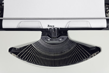 Old retro obsolete white typewriter with close-up typing text News as heading on paper