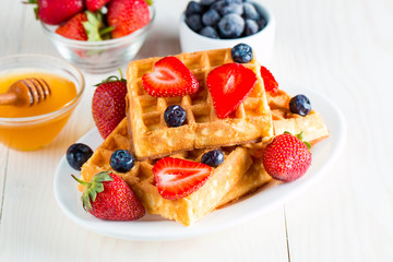 Photo of fresh homemade food made of berry Belgian waffles with honey, chocolate, strawberry, blueberry, maple syrup and cream. Healthy dessert breakfast concept with juice. 