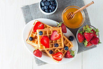 Photo of fresh homemade food made of berry Belgian waffles with honey, chocolate, strawberry, blueberry, maple syrup and cream. Healthy dessert breakfast concept with juice. 