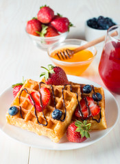 Photo of fresh homemade food made of berry Belgian waffles with honey, chocolate, strawberry, blueberry, maple syrup and cream. Healthy dessert breakfast concept with juice. 