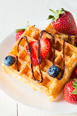 Photo of fresh homemade food made of berry Belgian waffles with honey, chocolate, strawberry, blueberry, maple syrup and cream. Healthy dessert breakfast concept with juice. 