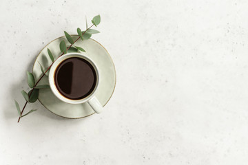 Cup of black coffee on a white textured table with a branch of eucalyptus. Top view, minimalism style, copy space.
