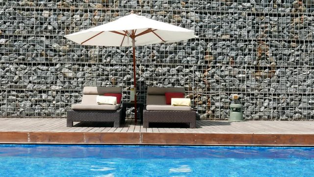Two pool beds lounge chairs and parasol against a stone wall next to a blue swimming pool.