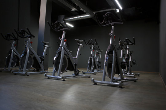 Modern Gym Interior With Equipment. Row Of Training Exercise Bikes Detail, Backlight. Healthy Lifestyle Concept