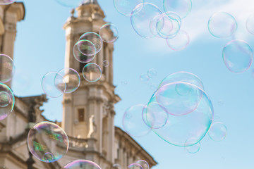 Closeup view of soap bubbles flying against the blue sky. Blurred famous church of Sant Agnes in Agona in the Navona Square is in the background.  Rome. Italy.