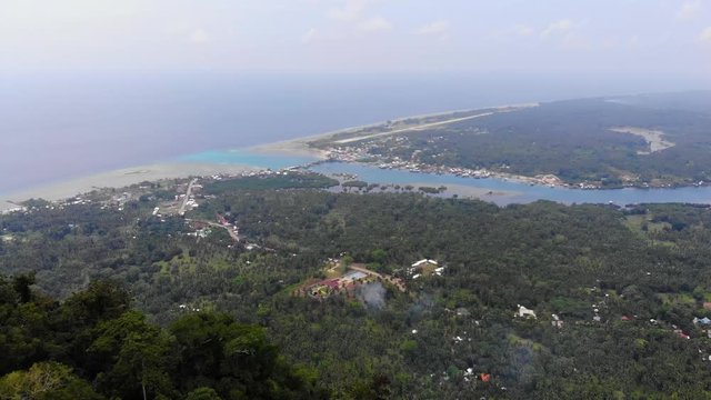 Wide aerial view of the coastline on Tawi Tawi, Philippines with the tiny landing strip for the airport in view. Lush tropical rainforest foliage on a hilltop and toward the interior of the island.