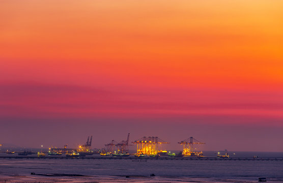 Crane At Dock Of Logistic Transportation At Harbor In Sea To Deliver Chemical And Industrial Product To Industrial Plant Onshore With Sunset Time