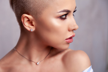 Closeup sexy blonde model with bright make-up, bare shoulders and short hair with shaved temples in modern round silver jewelry earrings and necklace. Сoncept shooting for bijouterie store