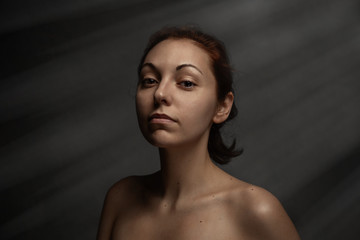Portrait of tan nude woman proudly looks on a camera. Dark background with the ray of light