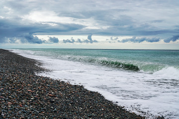 Pebble beach on the black sea. Beautiful clouds over the sea before the rain. Surf wave. Abkhazia. Georgia.