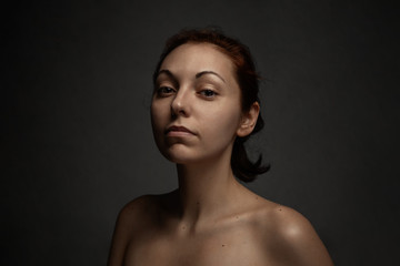 Portrait of tan nude woman proudly looks on a camera. Dark background