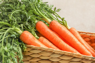 Wicker basket with ripe carrots against light, closeup