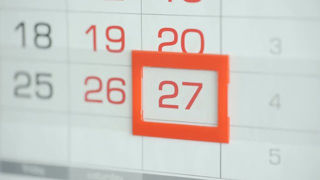 Woman's hand in office changes date at wall calendar. Changes 26 to 27