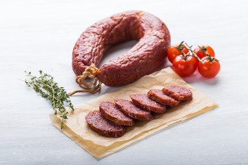 Food, cuisine and horsemeat concept - Close up of meat sausage with tomatoes and pepper on kraft paper
