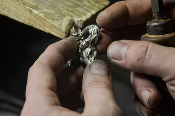 The master jeweler holds the working tool in his hands and makes jewelery at his workplace in the jewelry workshop.