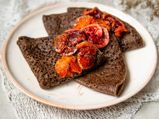 Thin chocolate pancakes with blood oranges sauce on a white plate on gray background with lace fabric. Stack of crepes, russian blin, Maslenitsa. Tasty breakfast. Close up, selective focus