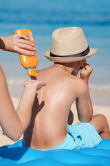Mom is covering her son with sunscreen on the beach during the summer holidays, preventing sun burns.