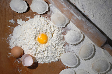 Flour is poured on a wooden kitchen table and it has egg yolk. Nearby are ready-made homemade dumplings, similar to shells. Studio light