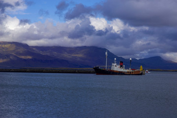 Obraz premium Ship against the backdrop of picturesque mountains and rain clouds entering the bay of the port of Reykjavik, Iceland