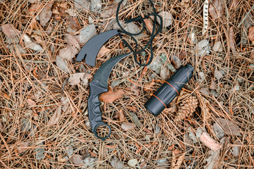 monocle and karambit knife on the ground covered with pine needles
