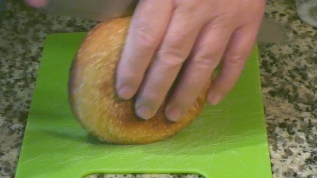 Breadknife cutting a freshly baked bread roll close up on a breadboard