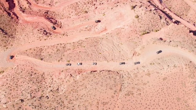 Wide aerial view of a group of off-road UTV vehicles climbing a red rock mountain in Moab, Utah.