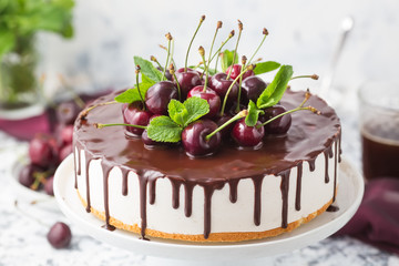 White mousse cake with vanilla base and chocolate topping decorated fresh cherries on a white cake stand. Summer dessert