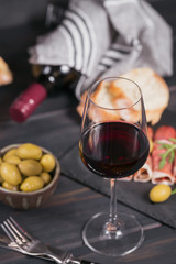 Glass of red wine with slices of cured ham or Spanish jamon serrano or Italian prosciutto crudo, bread, green olives and arugula