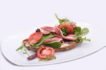 Top view Ham sandwich with tomatoes and herbs. Dark bread on a white background.