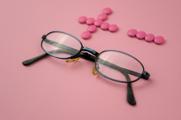 Glasses with plus and minus made of pills on pink background. Concept of eyesight correction