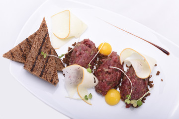 Meat tar tar with toasts, yolk, greens. On a white plate, on a white background