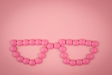 Face with glasses made of pink pills on pink background with vignette effect. Concept of eyesight
