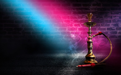 Hookah with smoke on the background of an empty brick wall, wet asphalt and colored neon light, blurry lights of the night city, bokeh