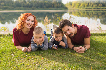 Parenthood, nature, people concept - family with two sons lying near the lake