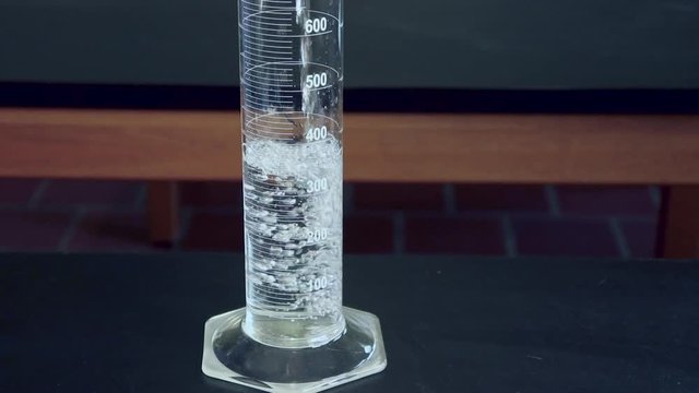 Close up of Clear liquid being poured into a 1000mL graduated cylinder on a black lab bench in a high school chimistry classroom