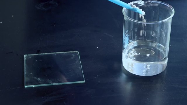Calcium metal being added to a glass beaker and reacting vigorouly with water to produce flamable hydrogen which is repeatedly lit by a burning splint