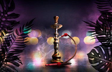 Hookah on the background of tropical leaves and a brick wall. Neon lights, laser shapes in the smoke, colorful bokeh
