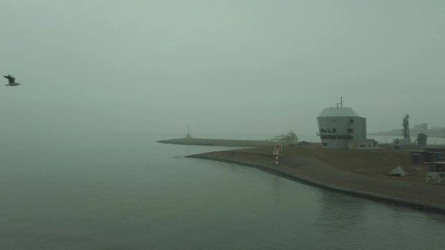 POV from a boat, showing the harbour area of Den Helder on an overcast day, military building on the isle.