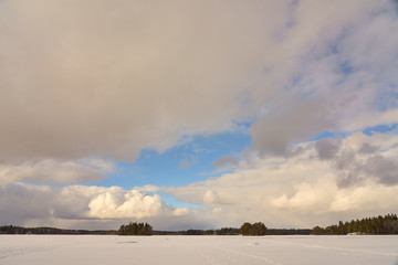 Obraz premium Two islands in the middle of Littoistenjärvi lake covered with ice and snow under a blue cloudy sky. Littoinen, Finland.