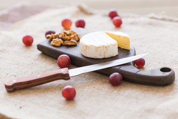 Brie or camembert cheese with nuts and grapes on a wooden board