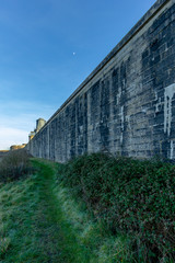 Fototapeta na wymiar A view a green grassy path along a huge fortress stone wall under a majestic blue sky